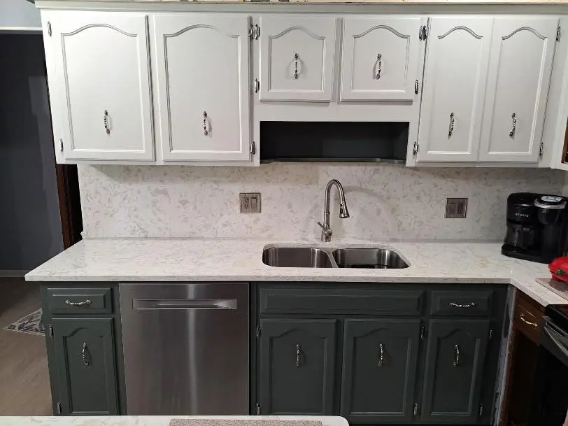 A kitchen with white upper cabinets and dark green lower cabinets, featuring a marble countertop and a built-in sink.