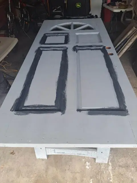 A pair of wooden doors painted gray, resting flat on a worktable in a cluttered garage.