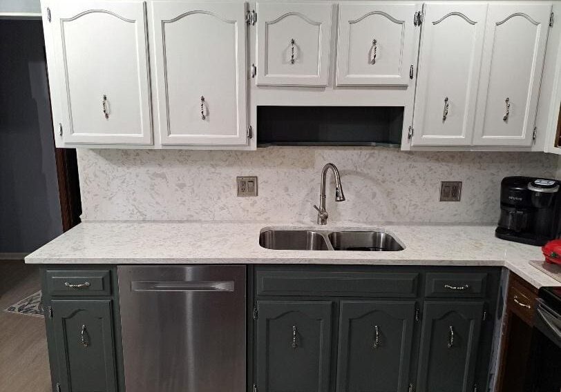 A kitchen with white upper cabinets and dark green lower cabinets, featuring a marble countertop and a built-in sink.